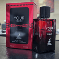 Maison Alhambra Your Touch Extrait — Red and black packaging with a chain design, next to a red glass perfume bottle with a black cap. | Pembungkusan merah dan hitam dengan rekaan rantai, bersebelahan botol minyak wangi kaca merah dengan penutup hitam.