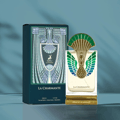 Maison Alhambra La Charmante by Maison Alhambra 100ml EDP — A perfume bottle with a gold and green peacock-inspired cap and ornate detailing on the front, displayed next to its matching dark teal box with art deco-inspired patterns and a deer emblem. | Maison Alhambra La Charmante by Maison Alhambra 100ml EDP — Botol