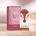 Maison Alhambra La Charmante Eclatant by Maison Alhambra 100ml EDP — A perfume bottle with a decorative fan-like gold and red atomizer sits next to its matching red and gold patterned box. | Maison Alhambra La Charmante Eclatant by Maison Alhambra 100ml EDP — Botol minyak wangi dengan penyembur emas dan merah seperti