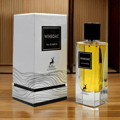 Maison Alhambra Winsome by Maison Alhambra 90ml EDP — A white box with black text and a deer logo sits next to a clear glass perfume bottle with yellow liquid and a black cap, displayed on a black and white tiered stand. | Maison Alhambra Winsome by Maison Alhambra 90ml EDP — Kotak putih dengan teks hitam dan logo