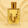Maison Alhambra Sugar Me Creme Brulee — A clear glass perfume bottle with a gold cap and a yellow and gold decorative front, next to its yellow and white striped box with a decorative gold frame containing the product name. | Maison Alhambra Sugar Me Creme Brulee — Botol minyak wangi kaca jernih dengan penutup emas
