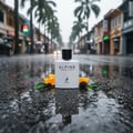 Maison Alhambra Alpine Homme Sport — White perfume bottle with black cap on wet asphalt, surrounded by orange slices, leaves, and pinecone, with palm trees and buildings in the background during rain. | Botol minyak wangi putih dengan penutup hitam di atas jalan basah, dikelilingi hirisan oren, daun, dan pokok pain