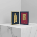 Maison Alhambra Renee Carmine EDP 100 ml Maison Alhambra — A gold perfume bottle displayed in a dark blue frame next to its matching dark blue and red box with gold accents. | Maison Alhambra Renee Carmine EDP 100 ml Maison Alhambra — Botol minyak wangi emas dipamerkan dalam bingkai biru gelap di sebelah kotak