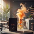 Maison Alhambra Toro Pour Homme – A bottle of Toro Pour Homme perfume with an orange smoke plume erupting from the top, next to its black box, set on a table in a cafe-like setting with plants and bar stools. | Maison Alhambra Toro Pour Homme – Sebotol minyak wangi Toro Pour Homme dengan kepulan asap oren meletus dari