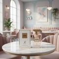 Maison Alhambra Como Moiselle — A perfume bottle and its box sit on a marble table in a cafe setting with pink velvet chairs and soft lighting. | Maison Alhambra Como Moiselle — Botol minyak wangi dan kotaknya terletak di atas meja marmar di suasana kafe dengan kerusi baldu merah jambu dan pencahayaan lembut.