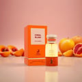 Maison Alhambra Coral Blush — An orange box and a perfume bottle are displayed with sliced fruits like peaches and grapefruits on a reflective surface against a pink background. | Maison Alhambra Coral Blush — Peti oren dan botol minyak wangi dipamerkan bersama hirisan buah-buahan seperti pic dan limau gedang di atas