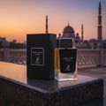 Maison Alhambra Dark Door Intense — A black box and a clear glass perfume bottle with a black label sit on a dark marble surface in front of a mosque at sunset. | Maison Alhambra Dark Door Intense — Sekotak hitam dan sebotol minyak wangi kaca jernih berlabel hitam terletak di atas permukaan marmar gelap di hadapan