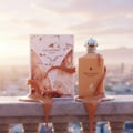 Maison Alhambra Decadent Wonder Her EDP 100 ml Alhambra — A perfume bottle and its box are displayed on a stone ledge, with caramel-like liquid dripping over them against a sunset sky. | Maison Alhambra Decadent Wonder Her EDP 100 ml Alhambra — Botol minyak wangi dan kotaknya dipamerkan di atas unjuran batu, dengan