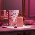 Maison Alhambra Decadent Dream – A pink perfume bottle and its box are displayed on a marble surface with rose petals, pearls, and a gold necklace. | Maison Alhambra Decadent Dream – Botol dan kotak minyak wangi berwarna merah jambu dipamerkan di atas permukaan marmar dengan kelopak mawar, mutiara, dan kalung emas.