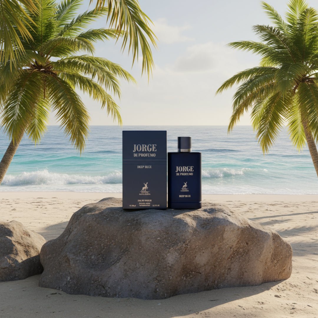 Maison Alhambra Jorge Di Profumo Deep Blue by Maison Alhambra 100ml Men — A dark blue perfume bottle and its box sit on a rock on a sandy beach with palm trees and the ocean in the background. | Maison Alhambra Jorge Di Profumo Deep Blue by Maison Alhambra 100ml Men — Botol dan kotak minyak wangi biru gelap diletakkan
