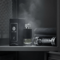 Maison Alhambra Encode By Maison Alhambra 100ml for Man — A black perfume bottle with a textured band and silver cap sits next to its matching box, with a dumbbell and folded towels in the background, wisps of steam rising. | Maison Alhambra Encode By Maison Alhambra 100ml for Man — Sebotol minyak wangi hitam dengan