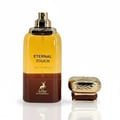 Maison Alhambra Eternal Touch by Maison Alhambra 80ml EDP — A clear glass perfume bottle with yellow and brown liquid, gold spray nozzle, and a separate gold cap with brown accents, set against a white background with reflection. | Maison Alhambra Eternal Touch by Maison Alhambra 80ml EDP — Botol kaca jernih berisi