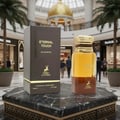 Maison Alhambra Eternal Touch — A dark brown perfume box and a golden-capped perfume bottle stand on a marble pedestal in a mall setting with palm trees and a golden dome | Maison Alhambra Eternal Touch — Kotak minyak wangi coklat gelap dan botol minyak wangi bertutup emas berdiri di atas alas marmar di latar pusat