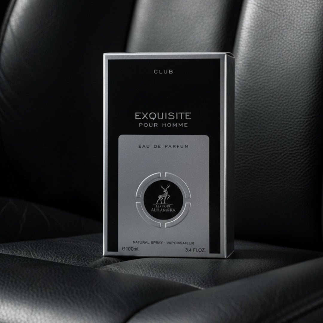 Maison Alhambra Exquisite Club By Maison Alhambra For Men 100ml — A black and silver perfume box with the text "EXQUISITE POUR HOMME" and a deer logo is placed on a dark, textured surface, possibly leather. | Maison Alhambra Exquisite Club By Maison Alhambra For Men 100ml — Kotak minyak wangi hitam dan perak dengan