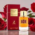 Maison Alhambra Exclusif Rose — Red box and gold-capped perfume bottle with amber liquid, surrounded by red roses on a reflective surface. | Maison Alhambra Exclusif Rose — Kotak merah dan botol minyak wangi bertutup emas dengan cecair ambar, dikelilingi mawar merah di permukaan reflektif.