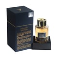 Maison Alhambra Exclusif Saffron – A dark blue box with gold accents and text, next to a clear glass perfume bottle with gold cap and amber liquid. | Maison Alhambra Exclusif Saffron – Kotak biru gelap dengan aksen emas dan teks, bersebelahan botol minyak wangi kaca jernih dengan penutup emas dan cecair ambar.