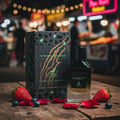 Extravagant Lover by Maison Alhambra – 100 ml – A perfume bottle and its box sit on a wooden surface with strawberries, blueberries, and rose petals scattered around. The background is a blurred night market with bokeh lights. | Extravagant Lover oleh Maison Alhambra – 100 ml – Botol minyak wangi dan kotaknya