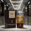 Maison Alhambra Flaming Elixir — A bottle of amber and burgundy Eau de Parfum stands next to its matching burgundy box with a white label. | Maison Alhambra Flaming Elixir — Sebotol Eau de Parfum berwarna kuning dan burgundy berdiri di sebelah kotak burgundy yang sepadan dengan label putih.