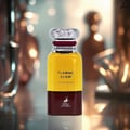Maison Alhambra Flaming Elixir — A bottle of amber and burgundy Eau de Parfum stands next to its matching burgundy box with a white label. | Maison Alhambra Flaming Elixir — Sebotol Eau de Parfum berwarna kuning dan burgundy berdiri di sebelah kotak burgundy yang sepadan dengan label putih.