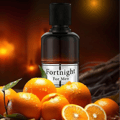 Maison Alhambra Fortnight by Maison Alhambra 100ml EDP Men — A dark glass perfume bottle with a black cap stands behind a cluster of wet oranges and orange slices, with a blurred warm background. | Maison Alhambra Fortnight by Maison Alhambra 100ml EDP Men — Botol minyak wangi kaca gelap dengan penutup hitam berdiri