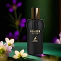 Maison Alhambra Glacier Le Noir — A black perfume bottle with a gold cap and gold text "GLACIER "LE NOIR" and a deer logo, set against a dark green background with blurred purple and white flowers. | Maison Alhambra Glacier Le Noir — Botol minyak wangi hitam dengan penutup emas dan teks emas "GLACIER "LE NOIR" serta