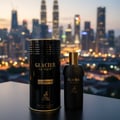 Maison Alhambra Glacier Le Noir — Black perfume bottle and cylindrical packaging stand on a dark surface with a blurred city skyline at dusk in the background. | Maison Alhambra Glacier Le Noir — Botol minyak wangi hitam dan pembungkusan silinder berdiri di atas permukaan gelap dengan latar belakang langit bandar yang