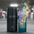 Maison Alhambra Glacier Pour Homme — Black cylindrical bottle next to a shattered teal bottle with colorful smoke erupting from it, set against a blurred parking garage background. | Maison Alhambra Glacier Pour Homme — Botol silinder hitam di sebelah botol teal yang pecah dengan asap berwarna-warni meletus
