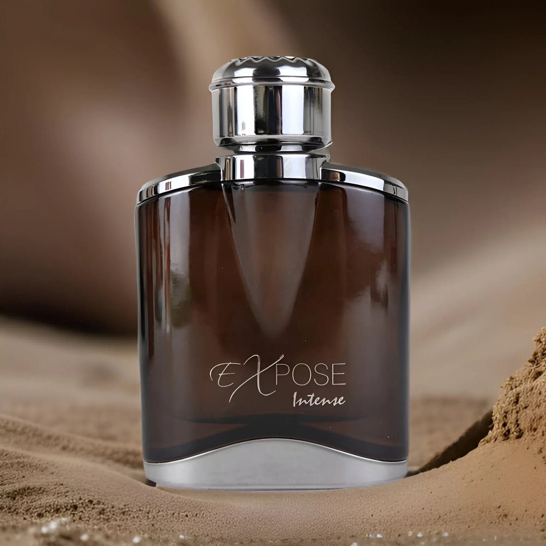 Maison Alhambra Expose Intense – A brown glass perfume bottle with a silver cap and accents, featuring the text 'Expose Intense' in white script, sits on a sandy surface with a blurred background. | Maison Alhambra Expose Intense – Botol minyak wangi kaca perang dengan penutup dan aksen perak, menampilkan teks 'Expose