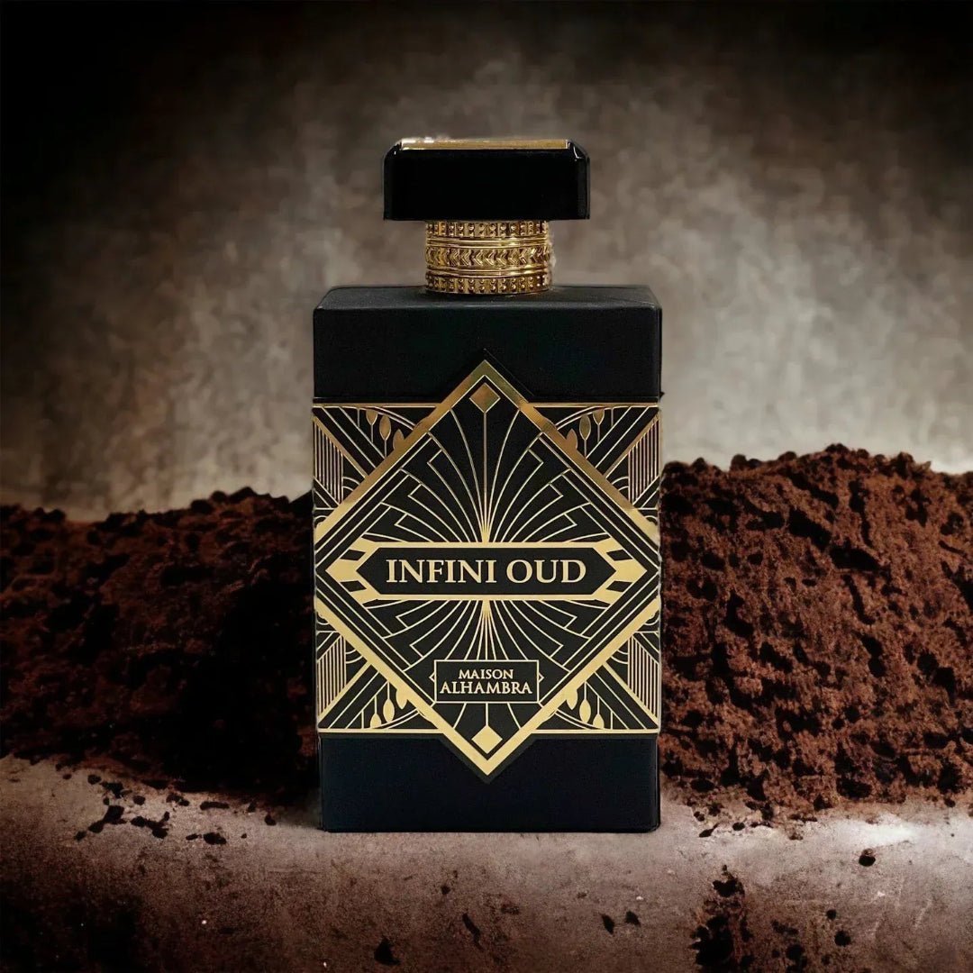 Maison Alhambra Infini Oud by Maison Alhambra Man 100ml EDP — A black perfume bottle with gold geometric art deco detailing and gold textured accents on the cap, placed on a surface with piles of dark brown powder on either side. | Maison Alhambra Infini Oud by Maison Alhambra Man 100ml EDP — Botol minyak wangi hitam