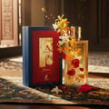 Maison Alhambra Renee Carmine EDP 100 ml Maison Alhambra — A perfume bottle and its box are displayed with vibrant orange and white flowers cascading around them, with red petals scattered on a patterned cloth. | Maison Alhambra Renee Carmine EDP 100 ml Maison Alhambra — Sebotol minyak wangi dan kotaknya dipamerkan