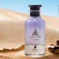 Maison Alhambra Jean Lowe Matiere — A clear glass perfume bottle with purple liquid, set on sand dunes with a blurred blue sky background. | Botol minyak wangi kaca jernih dengan cecair ungu, diletakkan di atas bukit pasir dengan latar belakang langit biru yang kabur.