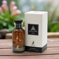 Maison Alhambra Jean Lowe Noir — A brown glass perfume bottle with a black cap and gold accents, placed next to its white and black box on a wooden surface with a blurred floral background. | Maison Alhambra Jean Lowe Noir — Botol kaca coklat dengan penutup hitam dan perincian emas, diletakkan di sebelah kotak putih