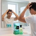 Maison Alhambra Jean Lowe Vibe by Maison Alhambra 100ml EDP — Man styling hair in front of a mirror with the perfume bottle and box on the counter | Maison Alhambra Jean Lowe Vibe by Maison Alhambra 100ml EDP — Lelaki menggayakan rambut di hadapan cermin dengan botol dan kotak minyak wangi di atas kaunter