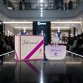 Maison Alhambra Just Married by Maison Alhambra Woman 100ml — A perfume box and bottle are displayed on a reflective surface in a mall setting. | Maison Alhambra Just Married by Maison Alhambra Woman 100ml — Kotak dan botol minyak wangi dipamerkan di permukaan reflektif dalam suasana pusat membeli-belah.