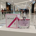 Maison Alhambra Just Married by Maison Alhambra Woman 100ml — A perfume bottle and its box are displayed on a white surface in a shopping mall corridor. | Maison Alhambra Just Married by Maison Alhambra Woman 100ml — Sebotol minyak wangi dan kotaknya dipamerkan di atas permukaan putih di koridor pusat membeli-belah.
