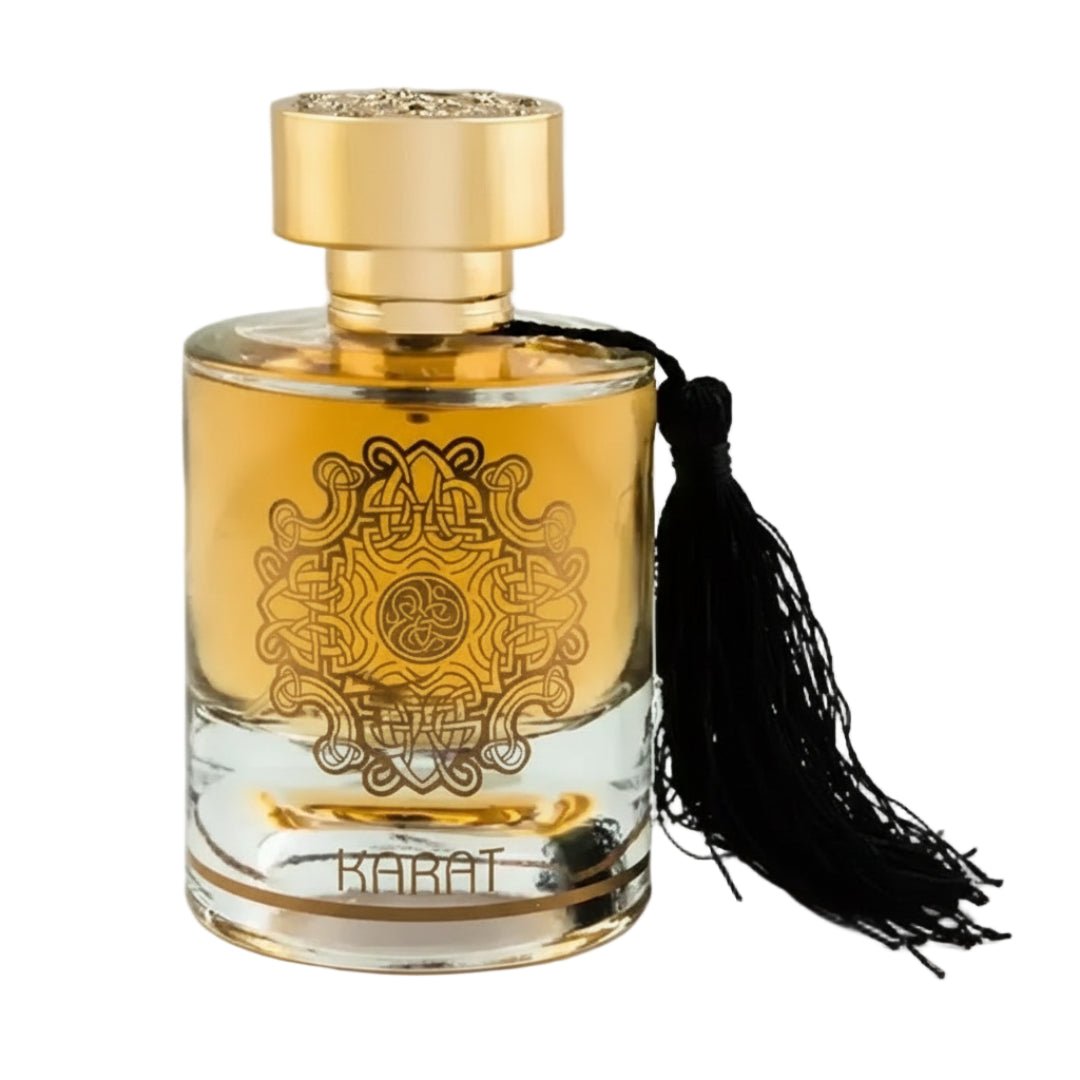 Maison Alhambra Karat by Maison Alhambra 100ml EDP — A clear glass perfume bottle with gold liquid, a gold cap, and a black tassel hanging from the neck, featuring a gold intricate knot design on the front and the word KARAT at the base. | Maison Alhambra Karat by Maison Alhambra 100ml EDP — Botol kaca jernih berisi