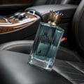 Maison Alhambra Kingsman – Blue glass perfume bottle with gold crown cap and gold emblem, next to a navy blue and gold striped box with matching emblem and deer graphic. | Maison Alhambra Kingsman – Botol minyak wangi kaca biru dengan penutup mahkota emas dan lambang emas, bersebelahan kotak berjalur biru navy dan