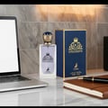Maison Alhambra Kingsman – Blue glass perfume bottle with gold crown cap and gold emblem, next to a navy blue and gold striped box with matching emblem and deer graphic. | Maison Alhambra Kingsman – Botol minyak wangi kaca biru dengan penutup mahkota emas dan lambang emas, bersebelahan kotak berjalur biru navy dan