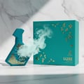 Maison Alhambra Luxe Emerald Perfume Maison Alhambra 100ml Unisex — Teal spray bottle with gold geometric pattern and smoke effect, next to its teal box with gold accents on a marble background. | Maison Alhambra Luxe Emerald Perfume Maison Alhambra 100ml Unisex — Botol semburan teal dengan corak geometri emas dan