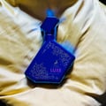 Maison Alhambra Luxe Nightlife — A blue perfume bottle with a geometric pattern and gold accents, resting on a golden, textured fabric. | Botol minyak wangi biru Maison Alhambra Luxe Nightlife dengan corak geometri dan aksen emas, diletakkan di atas fabrik bertekstur keemasan.