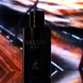 Maison Alhambra Salvo Elixir — Black glass perfume bottle with "SALVO ELIXIR" and a deer logo visible, set against a blurred, colorful, abstract background with diagonal light streaks. | Maison Alhambra Salvo Elixir — Botol kaca hitam dengan tulisan "SALVO ELIXIR" dan logo rusa kelihatan, berlatar belakang abstrak