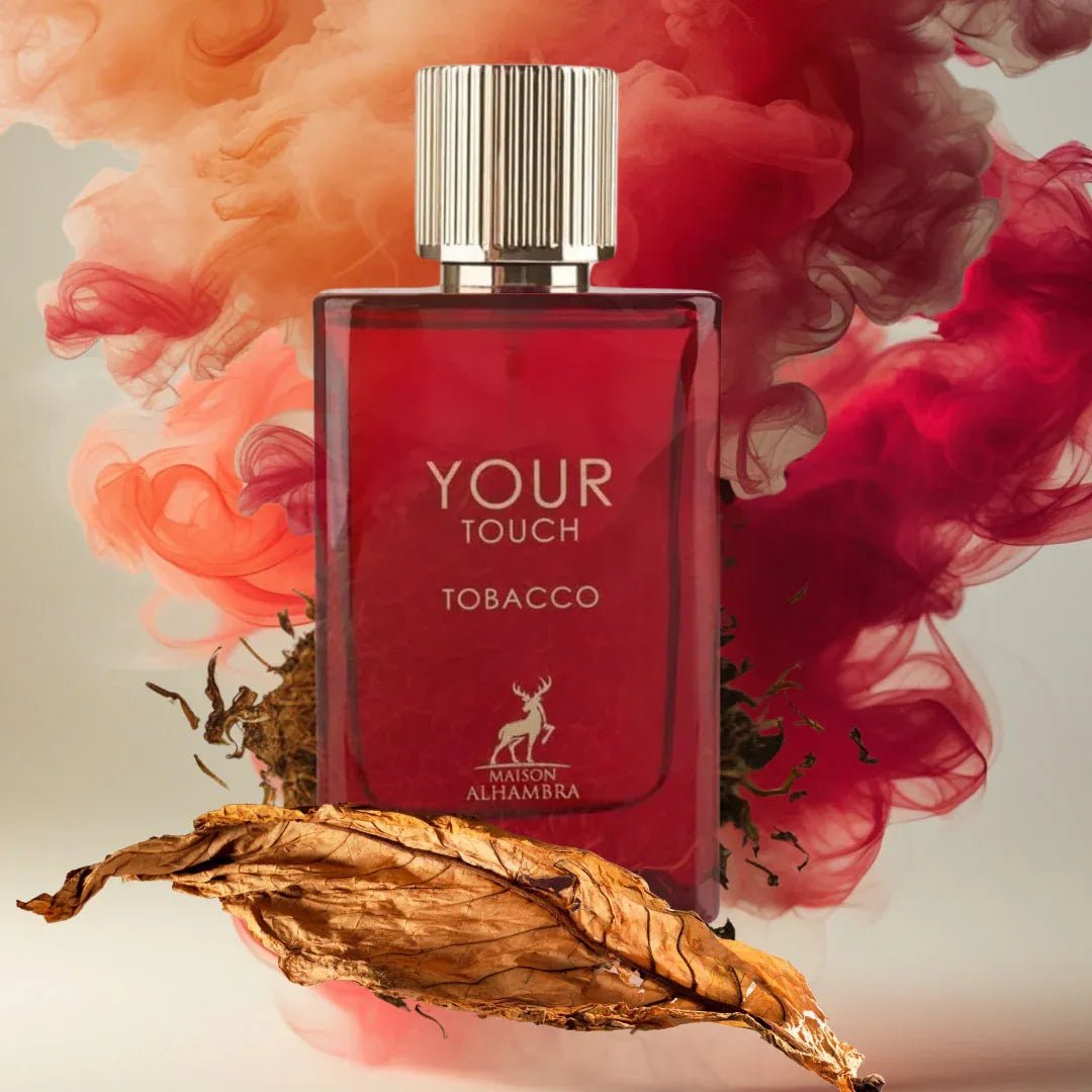 Maison Alhambra Tobacco Your Touch — A red glass perfume bottle with a fluted gold cap stands amidst swirling red and orange smoke, with a dried tobacco leaf in the foreground and loose tobacco leaves scattered around. | Maison Alhambra Tobacco Your Touch — Botol kaca merah dengan penutup emas bergalur berdiri di