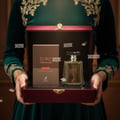 Maison Alhambra Toro Pour Homme Glace – A man's hand presents a luxurious gift box containing a perfume bottle and its matching box, with decorative gold embroidery on a green velvet dress. | Maison Alhambra Toro Pour Homme Glace – Tangan lelaki membentangkan kotak hadiah mewah yang mengandungi botol minyak wangi dan
