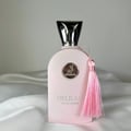 Maison Alhambra Delilah Pour Femme EDP 100ml – Women’s Perfume — A light pink perfume bottle with a silver emblem and a pink tassel hanging from the cap, set against a white satin background. | Maison Alhambra Delilah Pour Femme EDP 100ml – Women’s Perfume — Botol minyak wangi merah jambu muda dengan lambang perak dan