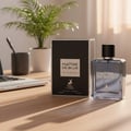 Maison Alhambra Maitre De Blue — A bottle of blue Eau de Parfum and its box sit on a wooden desk next to a laptop and a potted plant. | Maison Alhambra Maitre De Blue — Sebotol Eau de Parfum biru dan kotaknya diletakkan di atas meja kayu bersebelahan dengan komputer riba dan pokok dalam pasu.