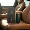 Maison Alhambra Sceptre Malachite — A green perfume bottle and its box sit on a tan leather car seat, with the car's interior visible in the background. | Maison Alhambra Sceptre Malachite — Botol minyak wangi hijau dan kotaknya diletakkan di atas tempat duduk kereta kulit berwarna tan, dengan bahagian dalam kereta