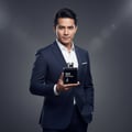 Maison Alhambra Man Black Edition Maison Alhambra 100ml EDP — A man in a dark blue suit and white shirt holds a black perfume bottle with silver accents. | Maison Alhambra Man Black Edition Maison Alhambra 100ml EDP — Seorang lelaki memakai sut biru gelap dan kemeja putih memegang botol minyak wangi hitam dengan