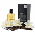 Maison Alhambra Montaigne Vanille — A clear glass perfume bottle with a black cap sits next to its black box, surrounded by white orchid flowers and dark vanilla pods. | Maison Alhambra Montaigne Vanille — Botol minyak wangi kaca jernih dengan penutup hitam terletak di sebelah kotak hitamnya, dikelilingi oleh bunga