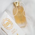 Maison Alhambra Musk Vanille by Maison Alhambra 100ml EDP — A frosted glass perfume bottle with a gold cap, adorned with a pearl necklace, sits next to its white and gold packaging box on a white fabric background. | Maison Alhambra Musk Vanille by Maison Alhambra 100ml EDP — Sebotol minyak wangi kaca beku dengan