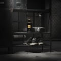 Maison Alhambra Black Origami by Maison Alhambra 100ml EDP — A black perfume bottle with a gold cap sits on a shelf next to a folded grey towel and a pair of black sneakers. | Maison Alhambra Black Origami by Maison Alhambra 100ml EDP — Botol minyak wangi hitam dengan penutup emas terletak di atas rak di sebelah tuala